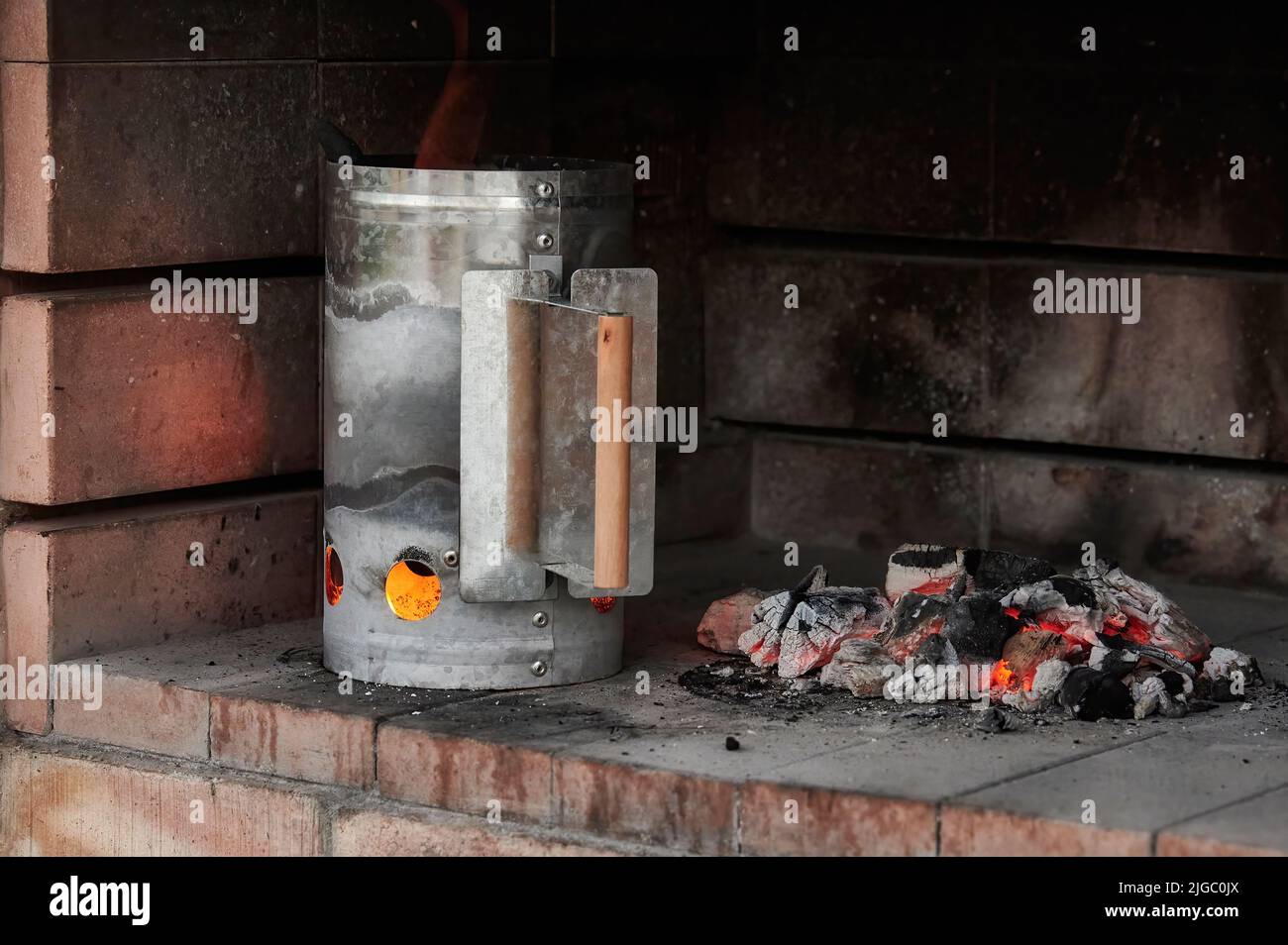 Charcoal Chimney Starter mit Feuer macht mehr Glut im Inneren des Grills, mit glühenden Kohle Glut daneben Stockfoto