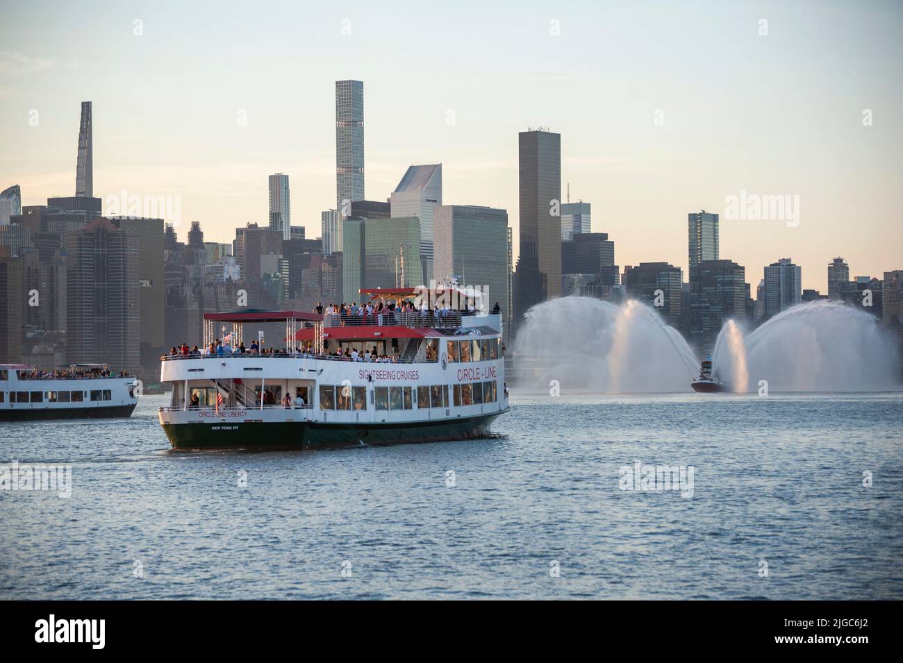 Mit einem Feuerboot, das Wasser in den Hintergrund sprühte, wartete ein Circle Line-Sightseeing-Boot auf dem East River auf den Beginn des Feuerwerks am 4. Juli. Stockfoto