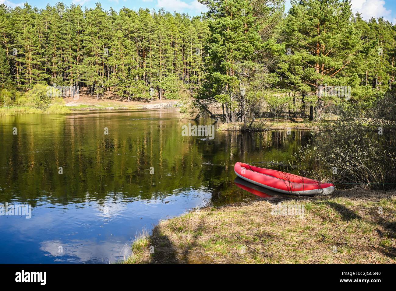 Rotes aufblasbares Kajak in der Nähe des Waldflusses. Frühlingswanderung zum Nationalpark. Stockfoto