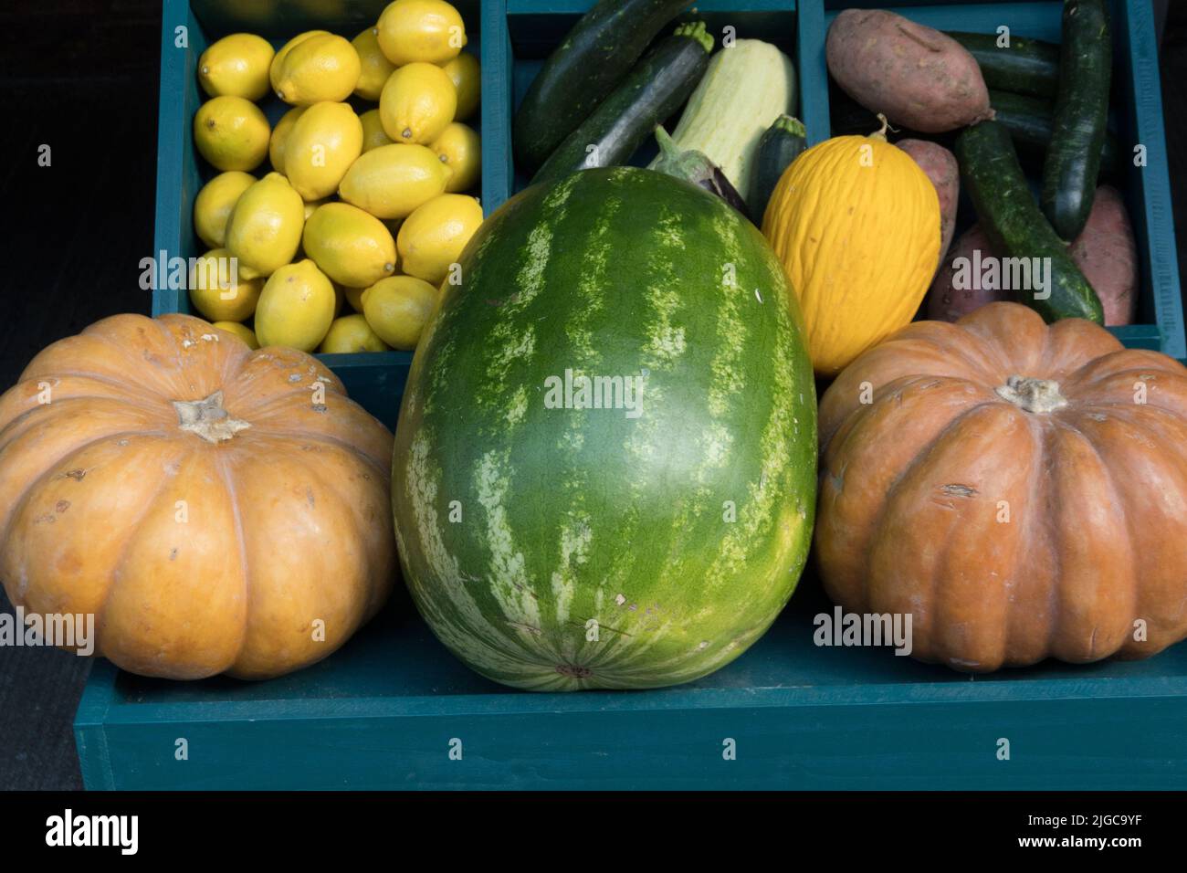 Zwei reife große Kürbisse neben einer großen Wassermelone im Verkaufsregal vor anderen Früchten und Gemüse wie Zuckerrüben Zitronen Zucchini und Hone Stockfoto