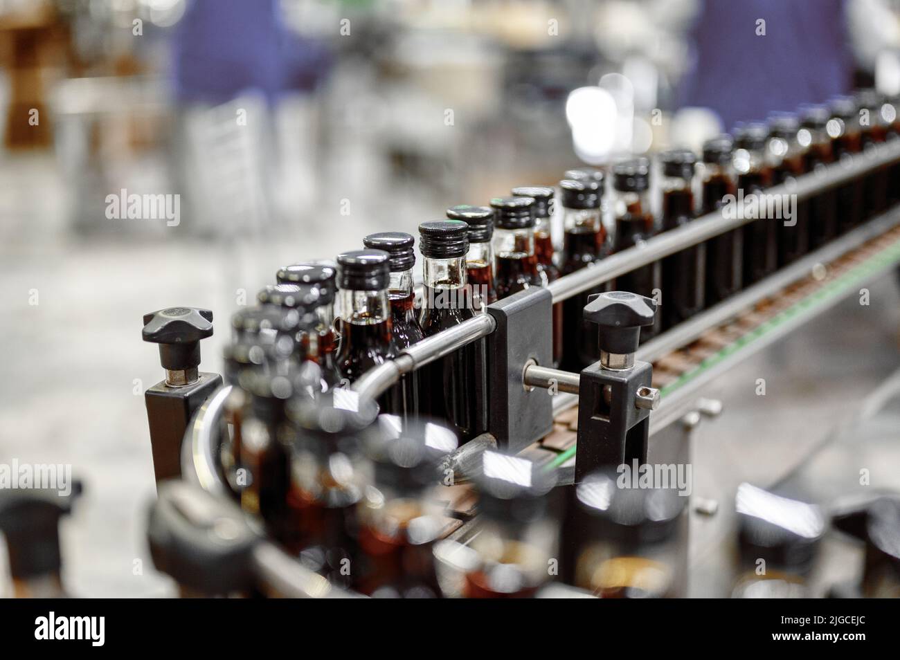 Glasflaschen mit dunkelrotem Alkohol, transportiert durch Förderband Stockfoto