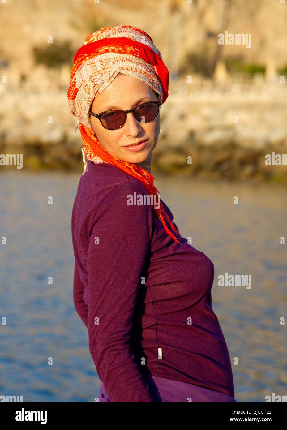 Reife Frau posiert in Puerto Rico Canary mit orangefarbenen Turban Sonnenbrille und burgunderroten Kleidung Stockfoto