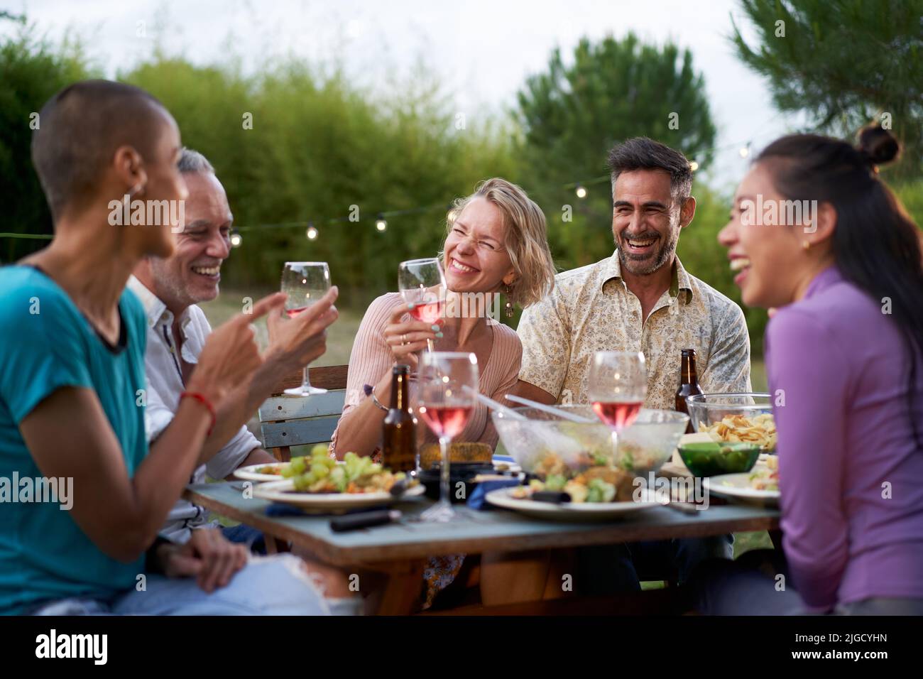 Fröhliche Männer und Frauen mittleren Alters, die beim Picknick auf dem Bauernhof gesundes Essen toasten - Life Style-Konzept mit fröhlichen Freunden, die am Nachmittag gemeinsam Spaß haben Stockfoto