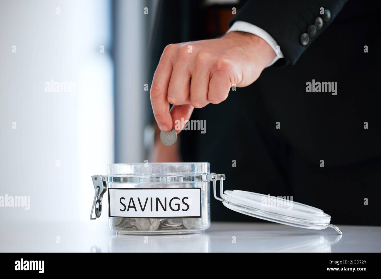 Geben Sie Ihr Geld nie aus, bevor Sie es haben. Ein unkennbarer Mann spart Münzen in einem Glas in einem Büro. Stockfoto