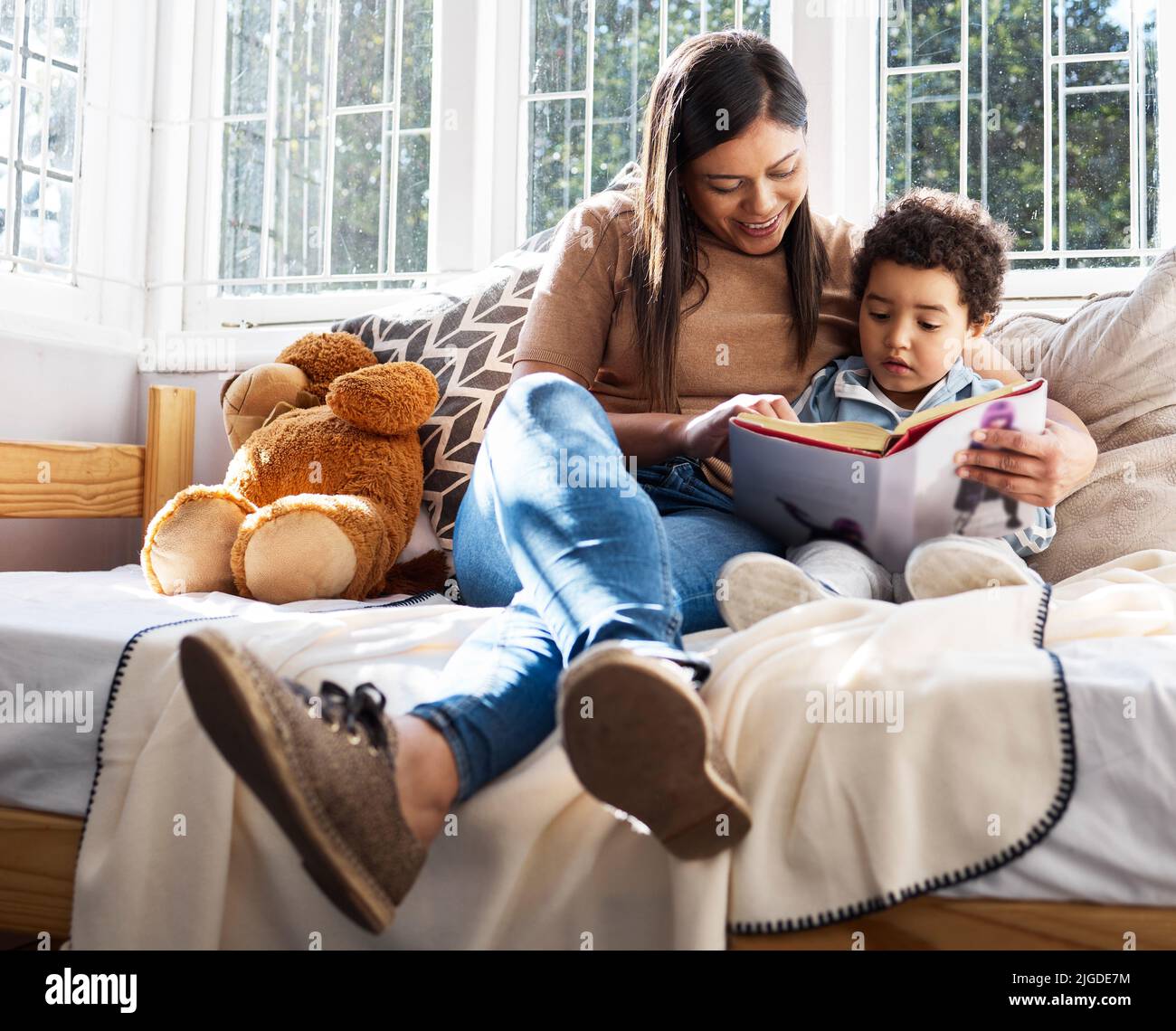 Eine junge Mutter und ein Sohn, die zu Hause zusammen ein Buch lesen, lesen es schon bald selbst. Stockfoto