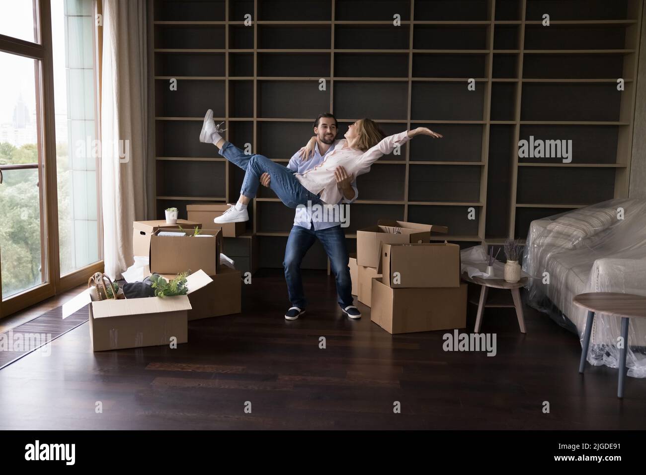 Glücklicher Hausbesitzer Kerl trägt Freundin in Armen im Wohnzimmer Stockfoto