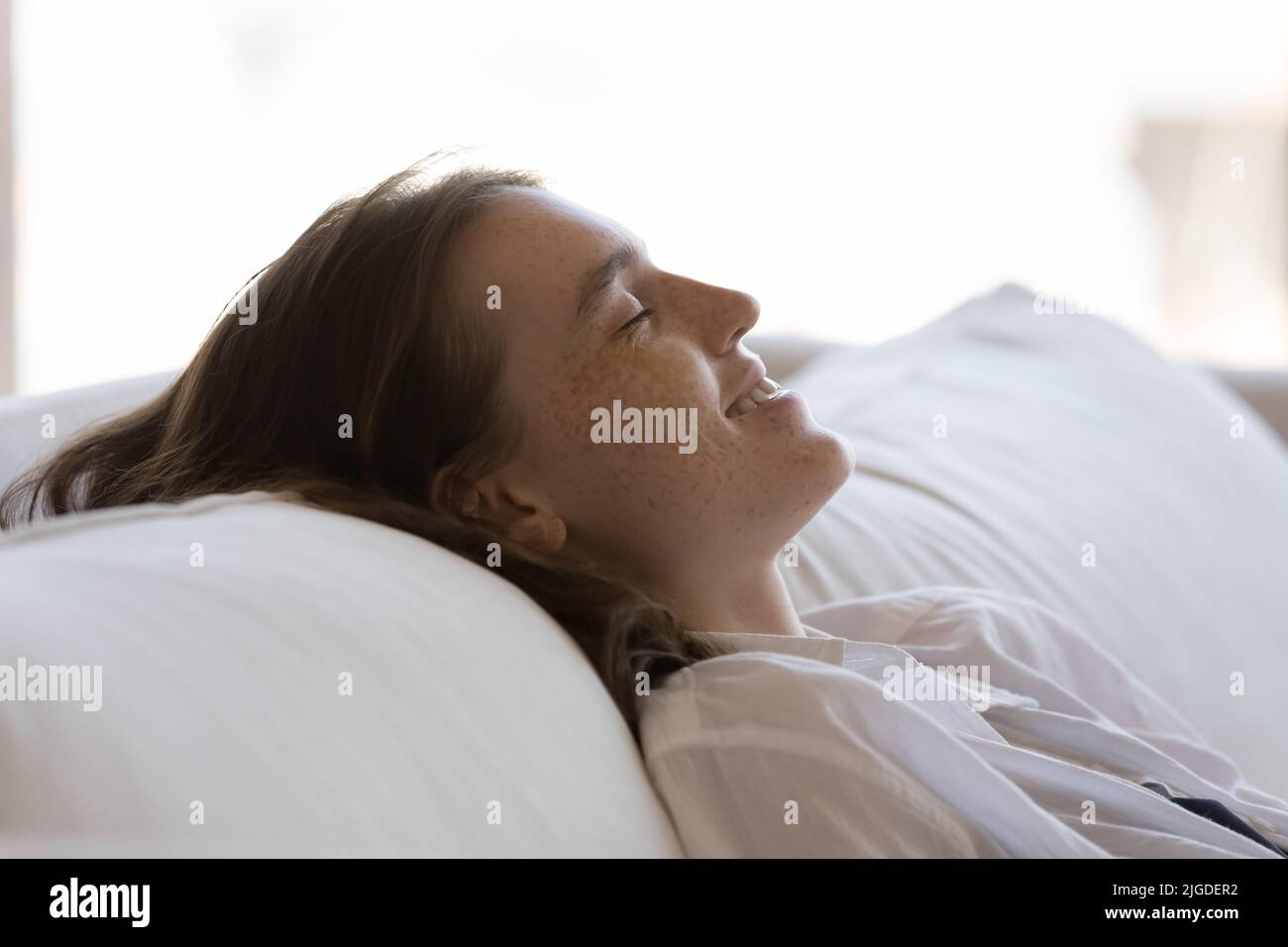 Junge Frau mit einem Lächeln und einem Lächeln entspannen sich auf dem gemütlichen Sofa aus nächster Nähe Stockfoto