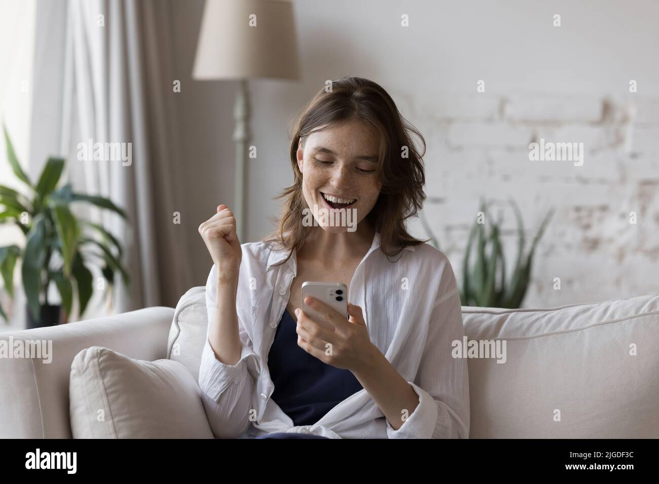 Junge Sommersprossen Frau hält Smartphone lesen gute Nachrichten fühlt sich überglücklich Stockfoto