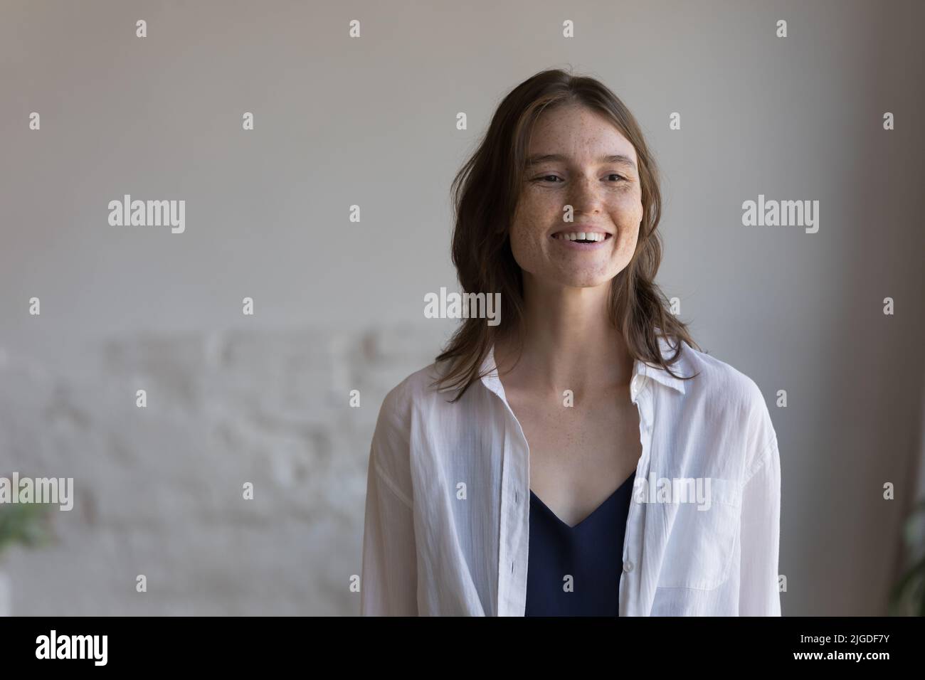 Lächelnde Frau mit niedlichen Sommersprossen auf attraktivem Gesicht posiert drinnen Stockfoto