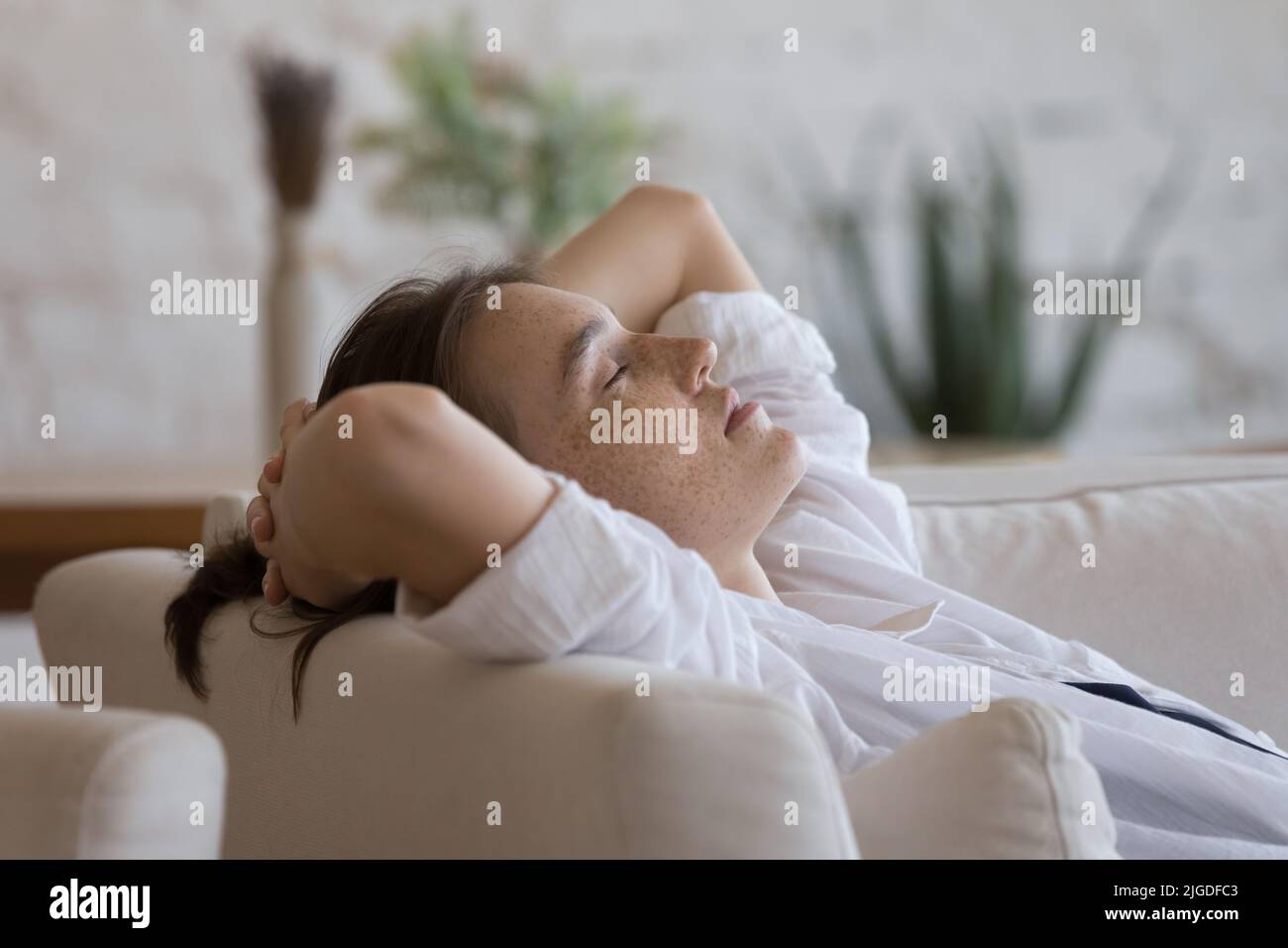Sommersprossen-Frau schläft auf dem Sofa mit den Händen hinter dem Kopf ein Stockfoto