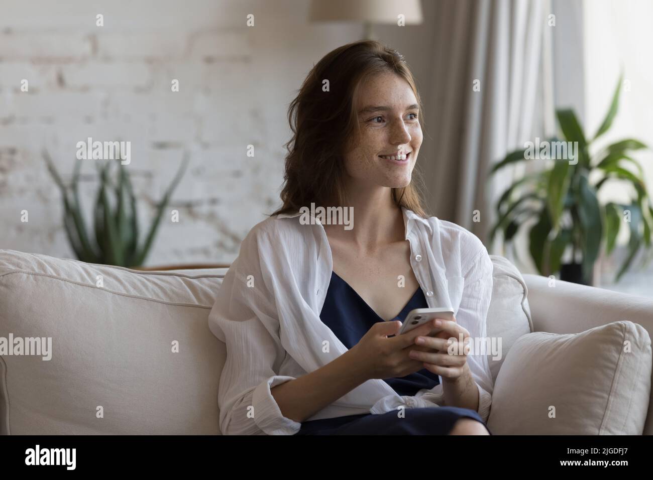 Junge Frau sitzt auf dem Sofa mit einem modernen Smartphone Stockfoto