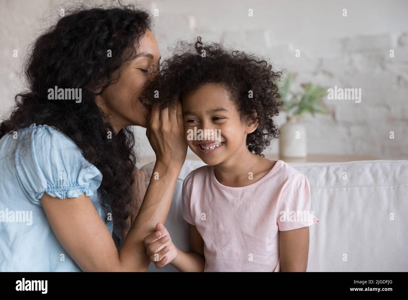 Die junge Mutter, die im Ohr flüstert, teilt das Geheimnis der lächelnden Tochter mit Stockfoto