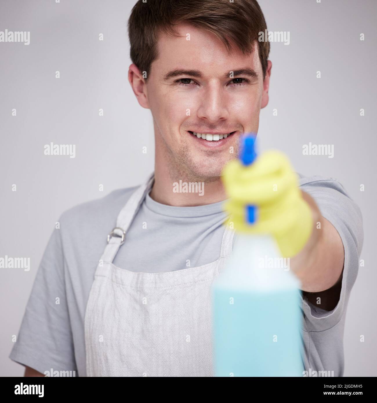 Keime haben nichts an diesem Produkt. Ein junger Mann hält eine Sprühflasche vor grauem Hintergrund. Stockfoto