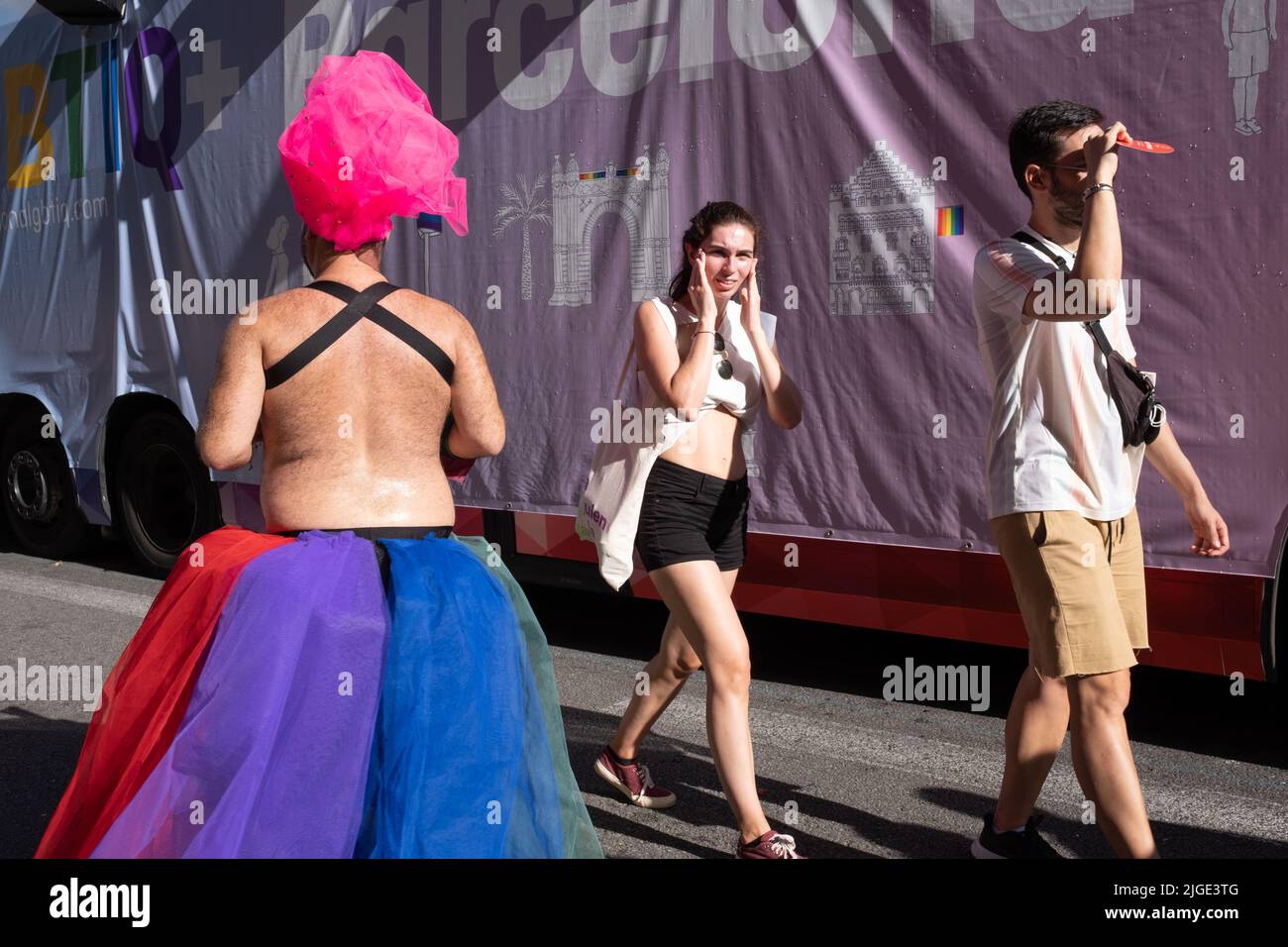 Barcelona, Spanien - 25. Juni 2022:Gay Pride 2022. Rückansicht eines Nachtschwärmers mit einem bizarren Kopfschmuck und zwei Touristen, die in die entgegengesetzte Richtung gehen Stockfoto