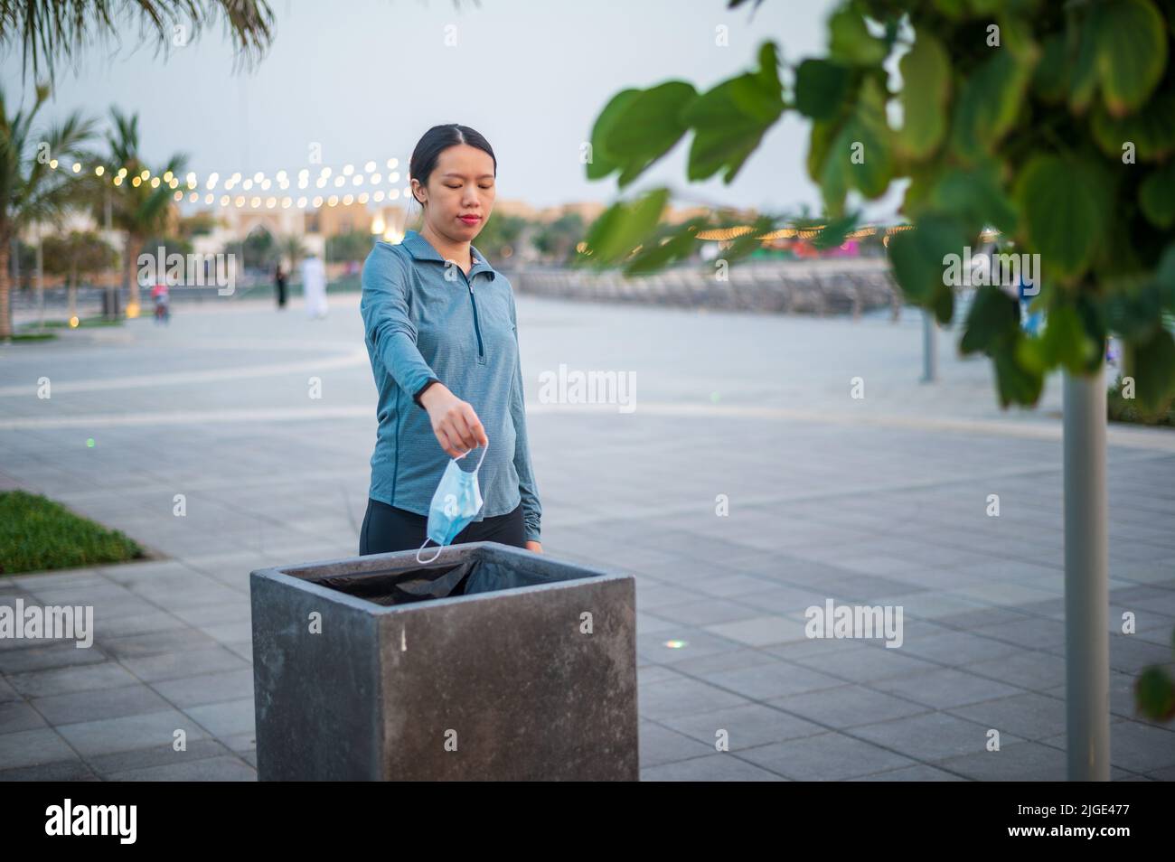 Asiatische Frau wirft eine gebrauchte chirurgische medizinische Gesichtsmaske in den Papierkorb im Freien Stockfoto