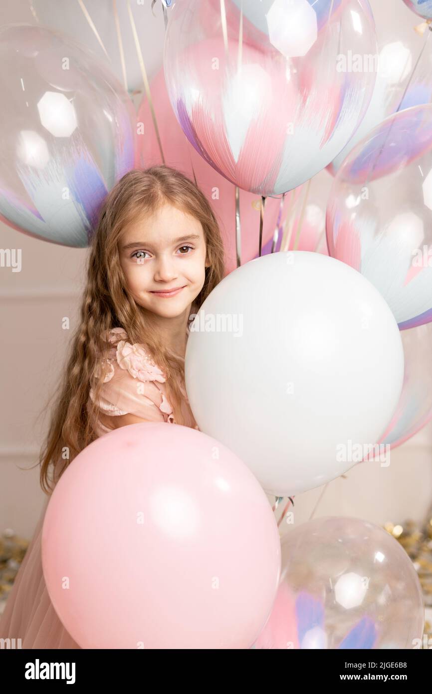 Glückliche Feier der Geburtstagsfeier mit Luftballons von charmanten niedlichen kleinen Mädchen im Kleid lächelnd zur Kamera auf rosa Hintergrund. Charmantes Lächeln, Ausdruck Stockfoto