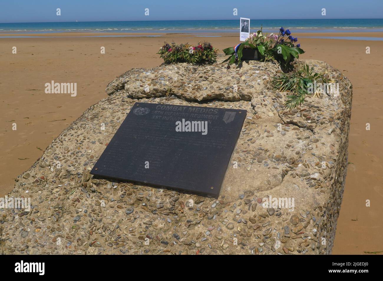 Blumen und ein Foto auf einem Gedenkstein erinnern an den 22-jährigen Mediziner Edward Morozewicz, der am 6. Juni 1944 in Omaha Beach getötet wurde, Arromanches-Les-Bains, Fra Stockfoto