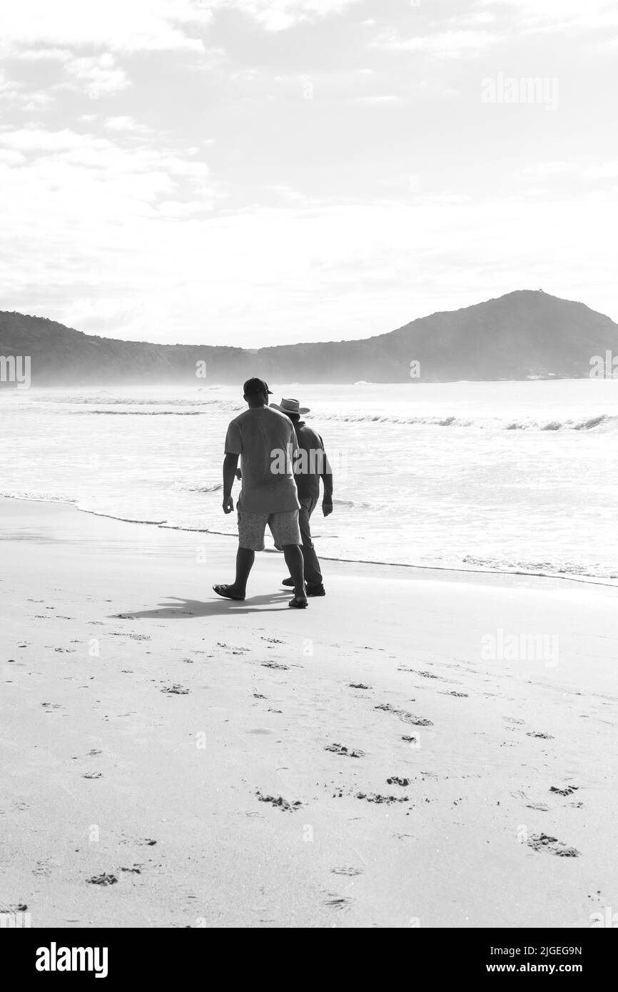 Schwarz-weiß-Foto von zwei Männern, die am Strand spazieren Stockfoto