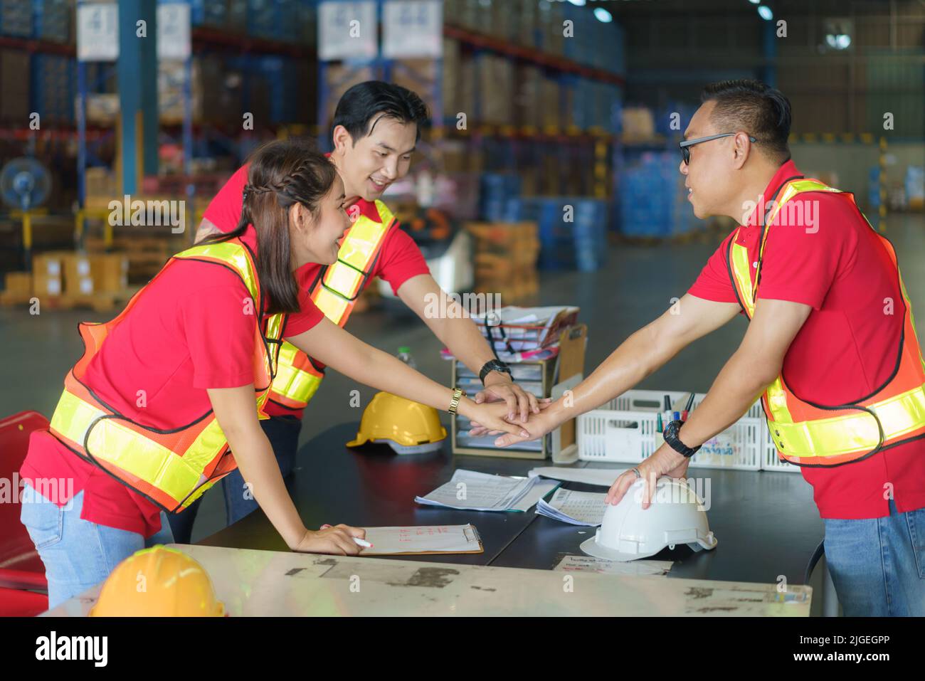 Einheit und Teamwork-Konzept. Das asiatische Arbeiterteam steht Hand an Hand und stapelt ihre Hand, bevor es im Lager arbeitet. Stockfoto
