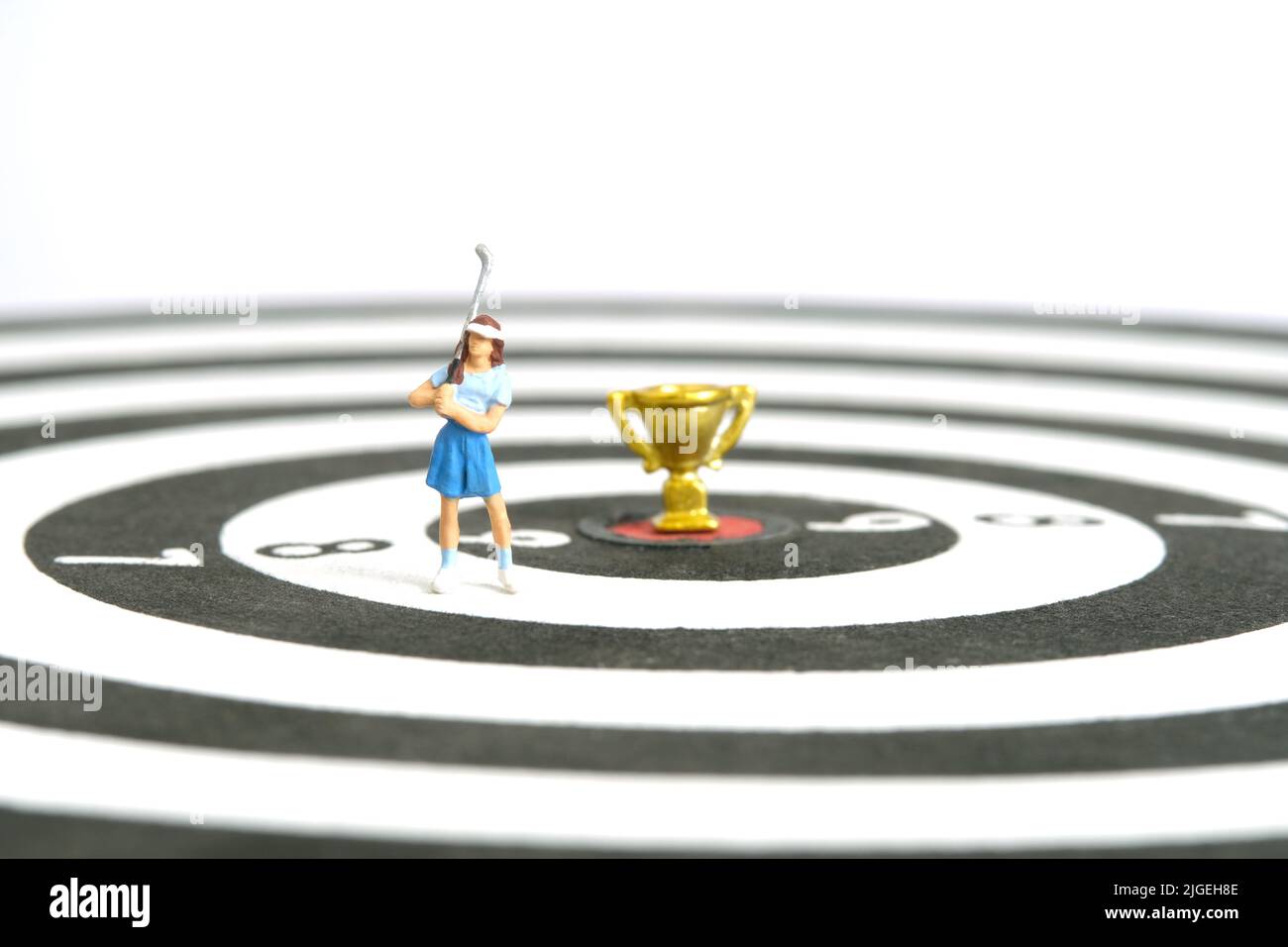 Miniatur Menschen Spielzeug Figur Fotografie. Ein Golfermädchen, das über der Dartscheibe mit Goldtrophäe in der Mitte steht, isoliert auf weißem Hintergrund. Bild-ph Stockfoto