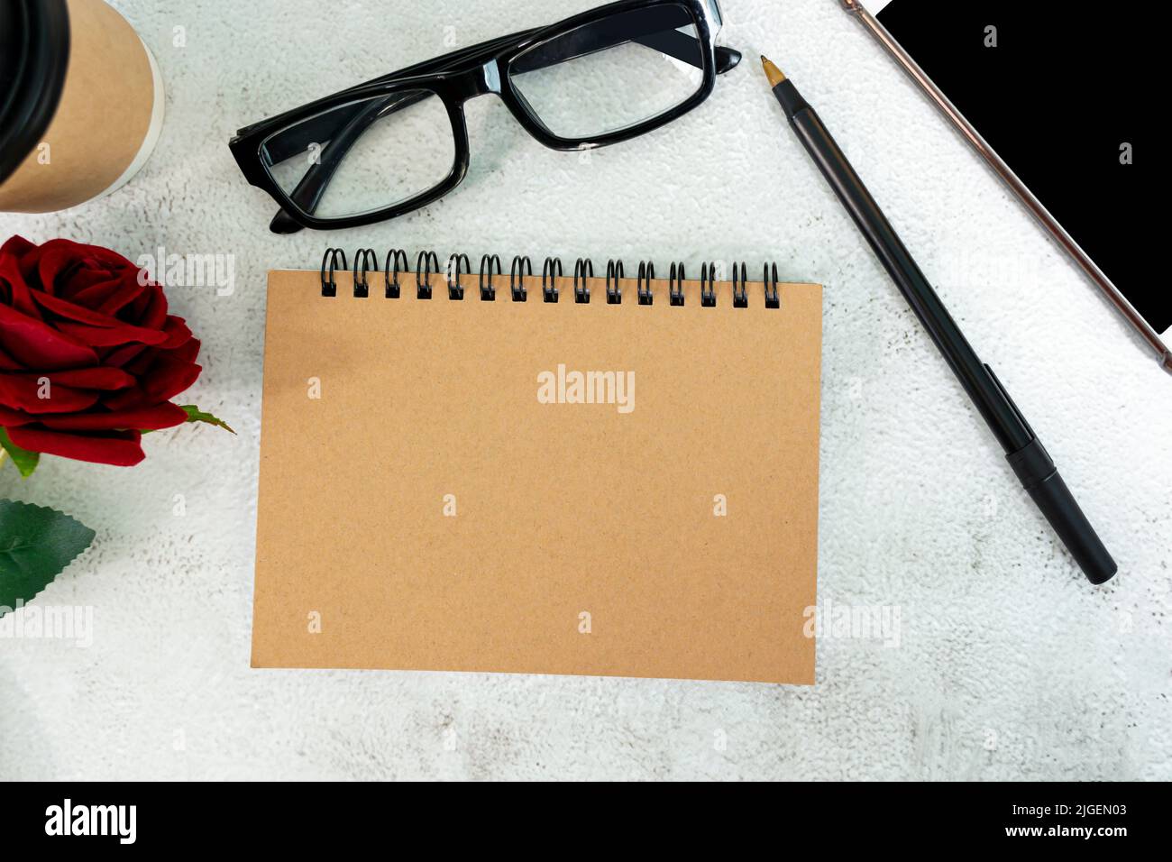 Braunes Notizbuch mit roten Rosen, Stift, Smartphone und Einweg-Kaffeetasse auf Marmorschreibtisch. Direkt darüber. Flach liegend. Speicherplatz kopieren. Stockfoto