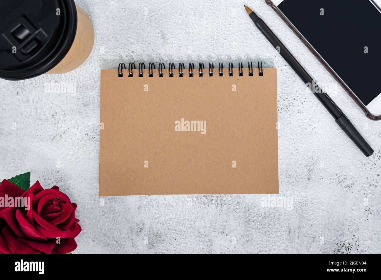 Braunes Notizbuch mit roten Rosen, Stift, Smartphone und Einweg-Kaffeetasse auf Marmorschreibtisch. Direkt darüber. Flach liegend. Speicherplatz kopieren. Stockfoto