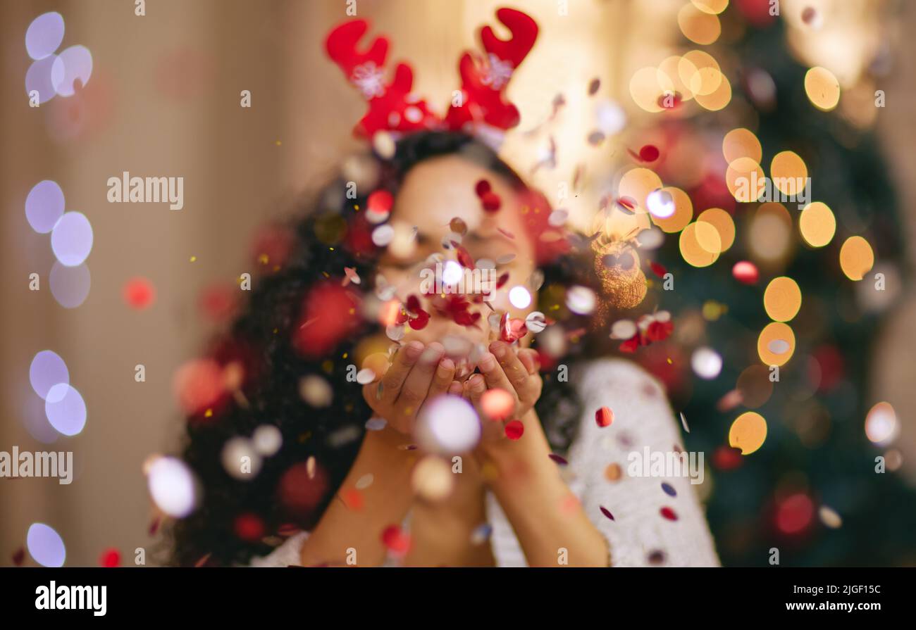 Eine junge Frau, die während der Weihnachtszeit zu Hause Konfetti bläst. Stockfoto