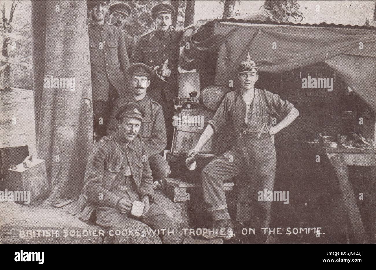 „Britischer Soldat kocht an der Somme mit Trophäen“: Foto mit britischen Soldaten an einer provisorischen Küche in einem Wald an der Westfront. Einer trägt einen deutschen Pickelhaube-Helm (ein anderer Soldat hält einen deutschen Helm im Hintergrund). Blechbecher, Mistdosen und Benzinkanister sind auch auf dem Bild zu sehen, das als Postkarte veröffentlicht wurde, die für den Blinded Soldiers Children Fund verkauft werden soll Stockfoto