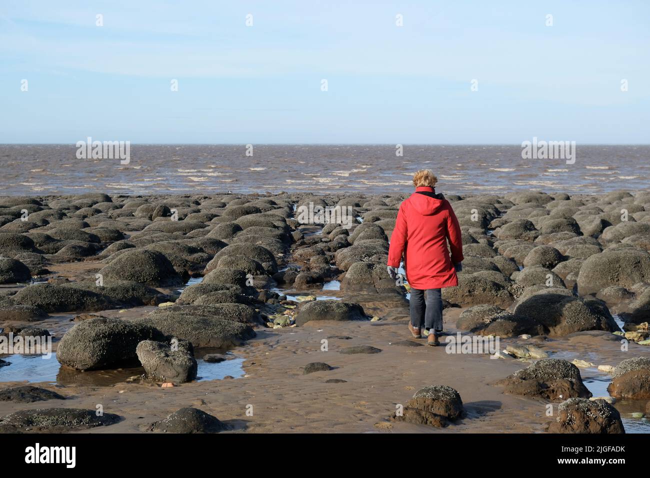 Frau in rotem Mantel am Hunstanton Beach bei Ebbe Stockfoto