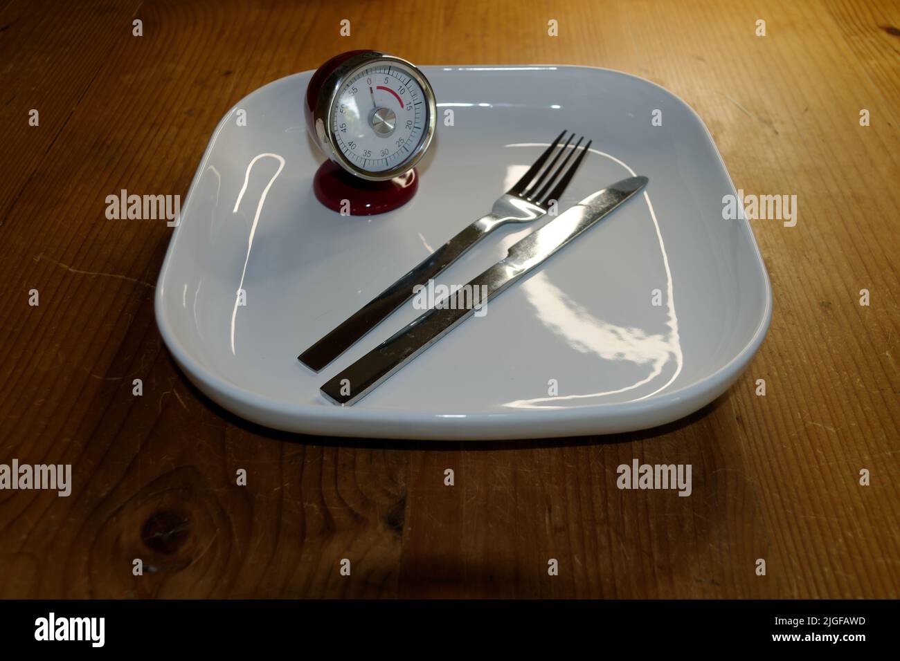 Symbolisches Bild für Ernährung und Gewichtskontrolle, Intervallfasten: Leerer Teller mit Stoppuhr und Messer und Gabel. Stockfoto