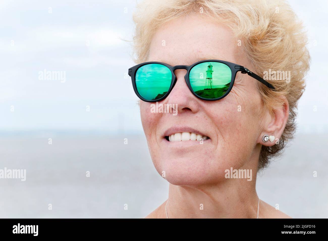 Ein Blick auf den Leuchtturm von Black Nore, Portishead, Großbritannien, spiegelt sich in der verschreibungspflichtigen Sonnenbrille einer Frau wider. Die Gläser sind in einem Oakley Pitchman R-Rahmen montiert Stockfoto