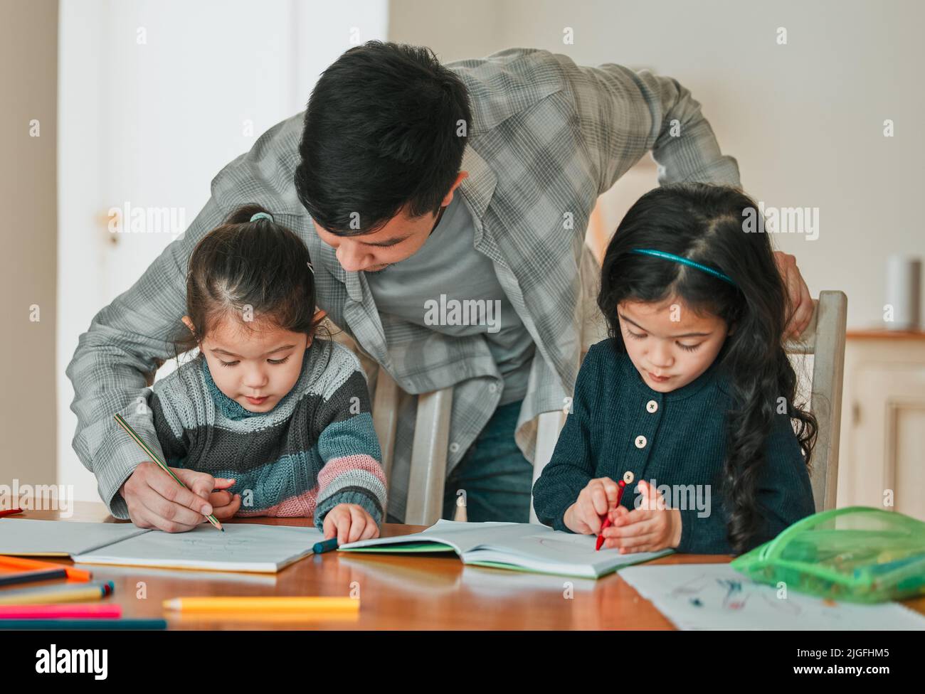 Wenn Sie diese beiden hinzufügen, was bekommen Sie: Ein junger Vater hilft seinen Töchtern bei ihren Hausaufgaben. Stockfoto