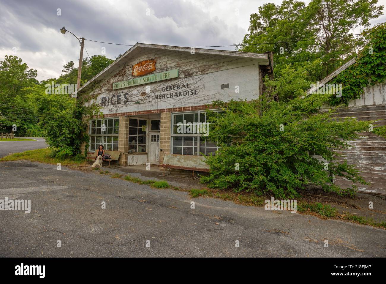Brevard, North Carolina, USA - 25. Juni 2022: Eine Frau und ihr Hund brüten vor einem alten Geschäft, das im ländlichen North Carolina verfällt. Stockfoto