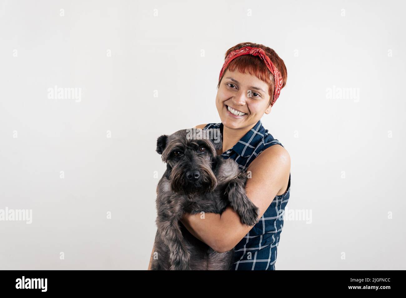 Eine lateinische Frau mittleren Alters, die einen Hund trägt Stockfoto