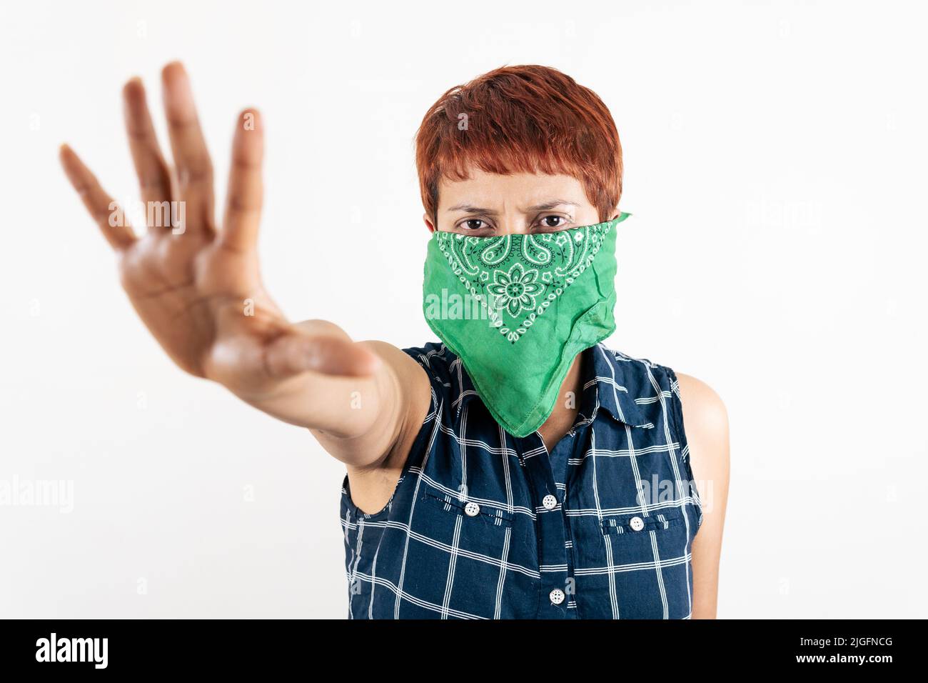 Eine lateinische Frau mittleren Alters bedeckt ihr Gesicht mit einem Schal und zeigt ihre Hand in einem Stoppschild Stockfoto