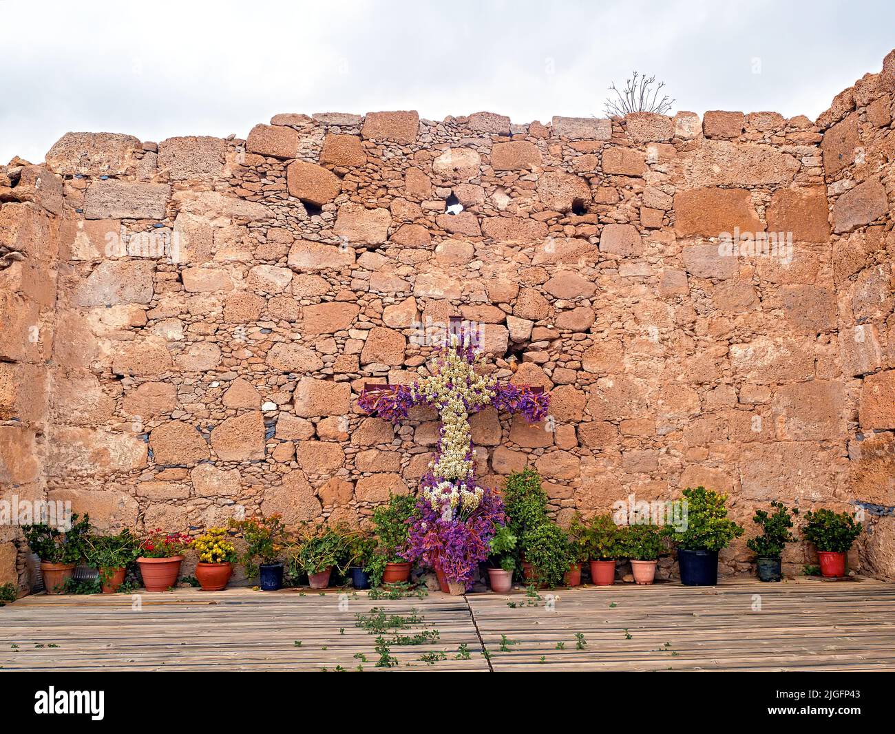 Eine zerbröckelnde antike Mauer einer alten Kirche im Süden von Teneriffa. Die Wand ist mit einem Blumenkreuz und verschiedenen Pflanzentöpfen verziert. Stockfoto