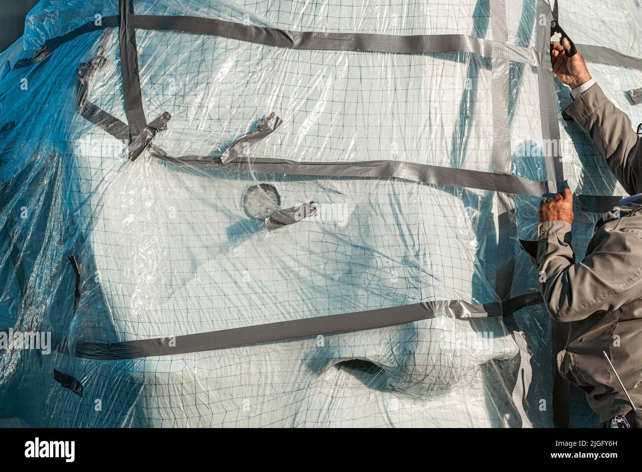 Ein Mann, der die Plastikfolie auf einer riesigen Kopfskulptur abschneidet Stockfoto