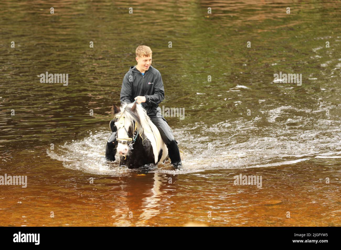 Ein Teenager, der auf seinem Pferd im Fluss Eden, auf der Appleby Horse Fair und auf der Appleby in Westmorland, Cumbria, reitet Stockfoto