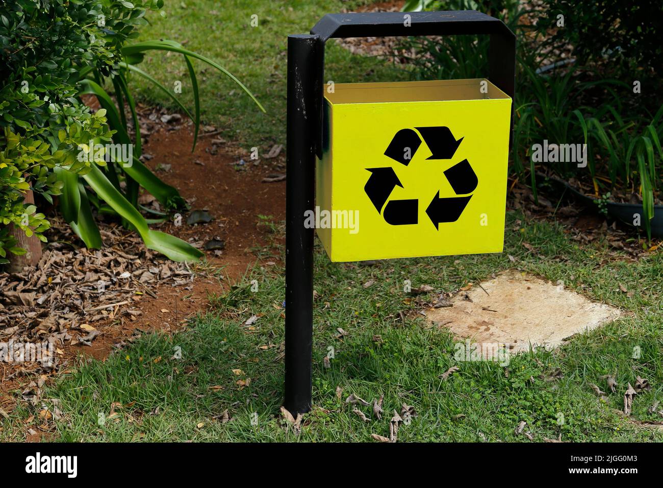 Gelber Metallabfallbehälter mit Recycling-Symbol im grünen öffentlichen Bereich und Garten - Müllabfuhr Stockfoto