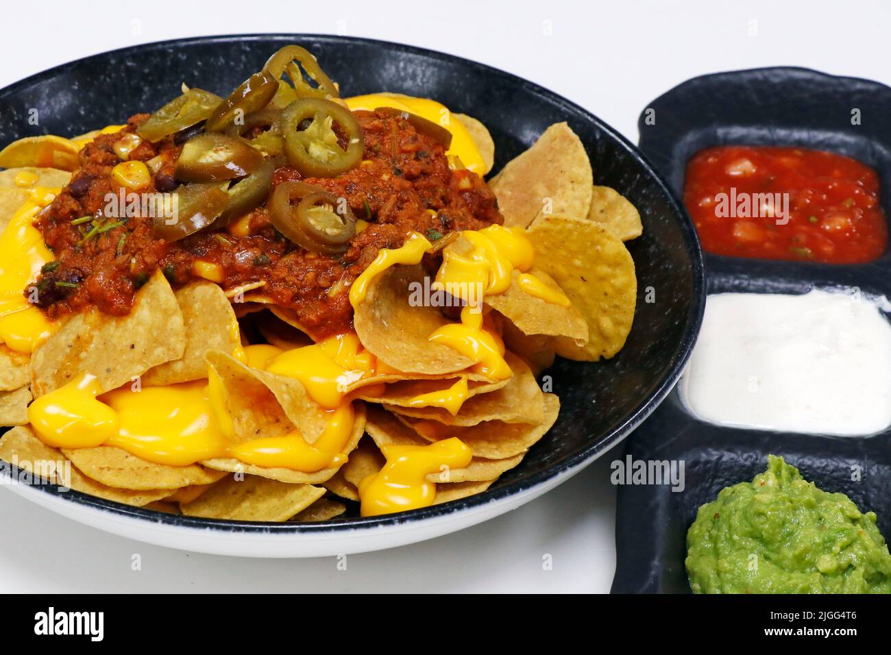 mexikanische Mais-Tortilla-Chips, bekannt als Nachos mit Avocado-Guacamole, saurer Creme, Tomatensalsa und Rindfleisch-Chili con Carne Stockfoto