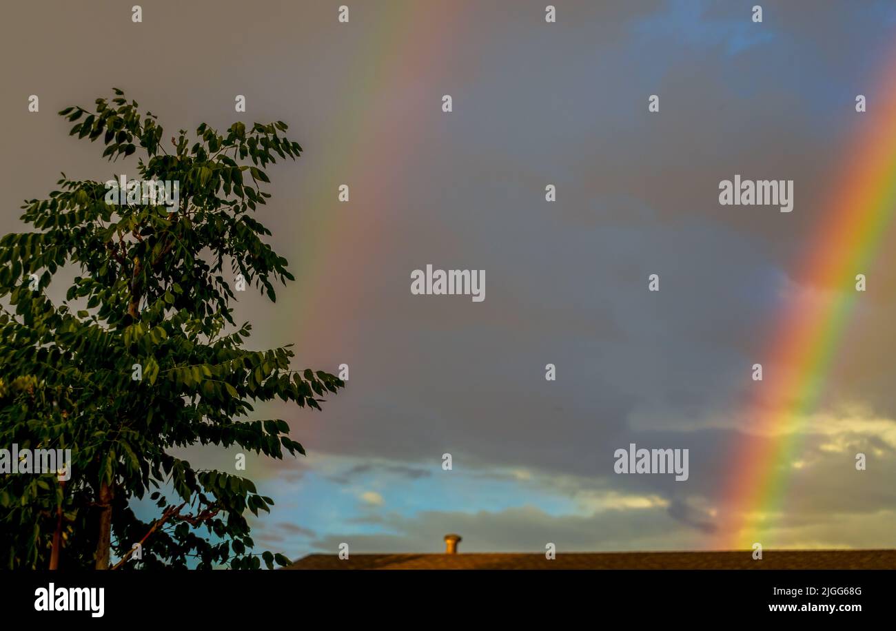 Doppelter Regenbogen nach dem Regen über dem Dach eines Landhauses und Bäumen in Aurora, Colorado Stockfoto