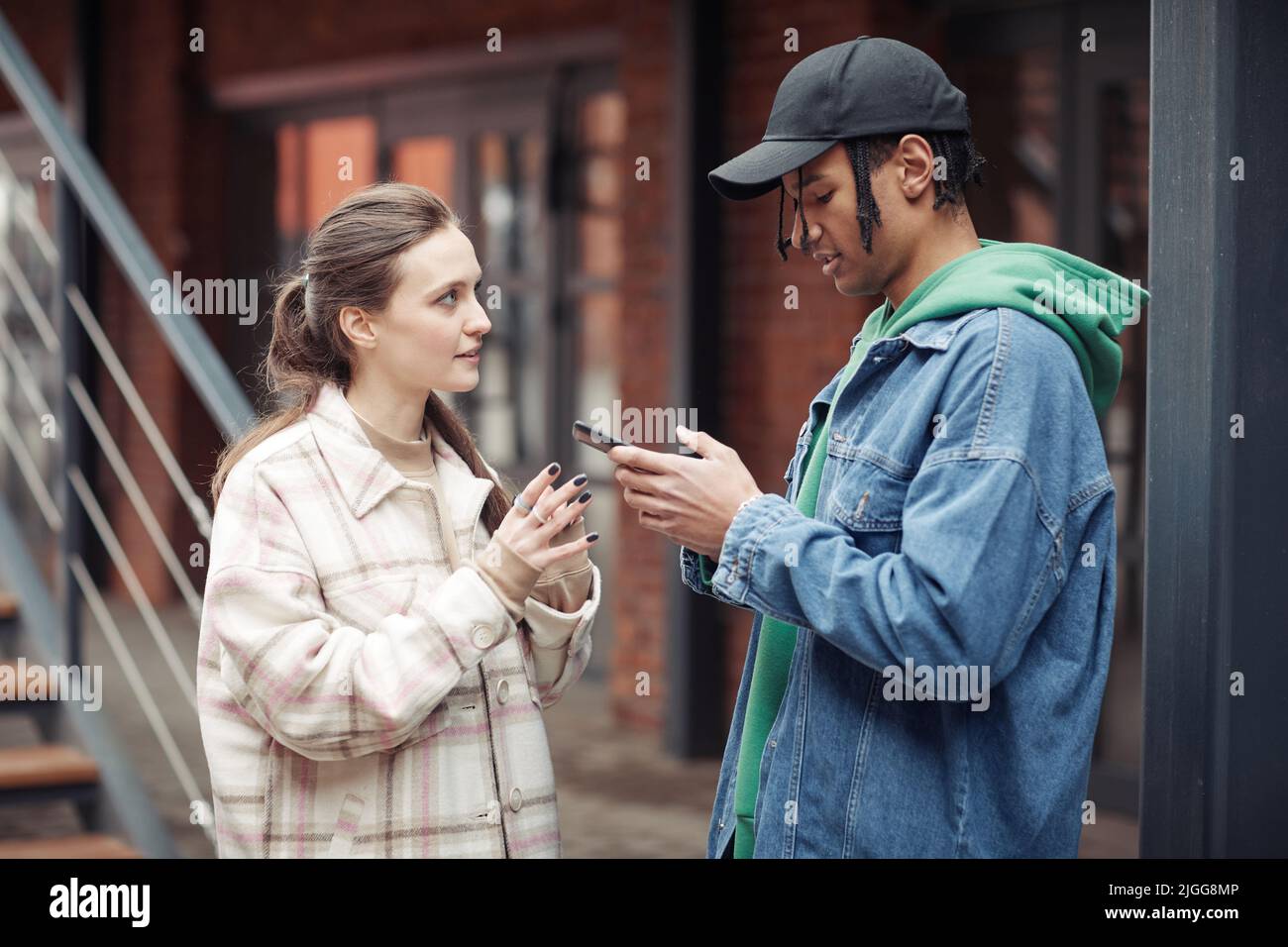 Seitenansicht eines Jugendlichen multikulturellen Paares in Casualwear, das sich unterhielt, während ein afroamerikanischer Mann auf der Straße per SMS auf dem Handy telefoniert Stockfoto