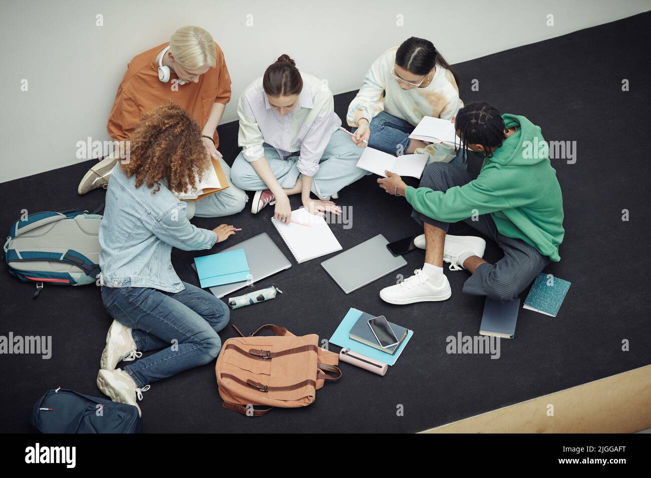 Über dem Winkel der Gruppe von multikulturellen Jugendlichen in der Freizeitkleidung diskutieren Vorlesungsnotizen nach dem Unterricht, während sie ihre Copybooks betrachten Stockfoto