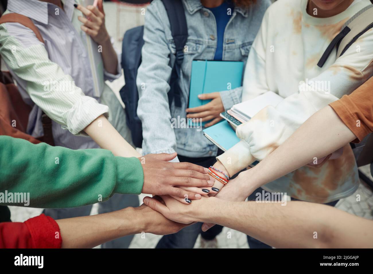 Eine Gruppe interkultureller Teenager-Studenten in Casualwear, die im Kreis stehend Handhaufen machen, um Unterstützung und Einheit zu symbolisieren Stockfoto