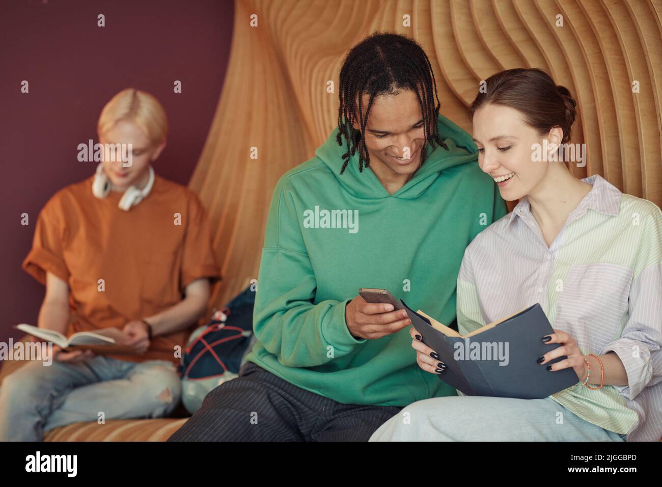 Happy interracial Teenager-Paar in Casualwear diskutieren Foto im Smartphone von afroamerikanischen Kerl in College-Korridor gehalten Stockfoto