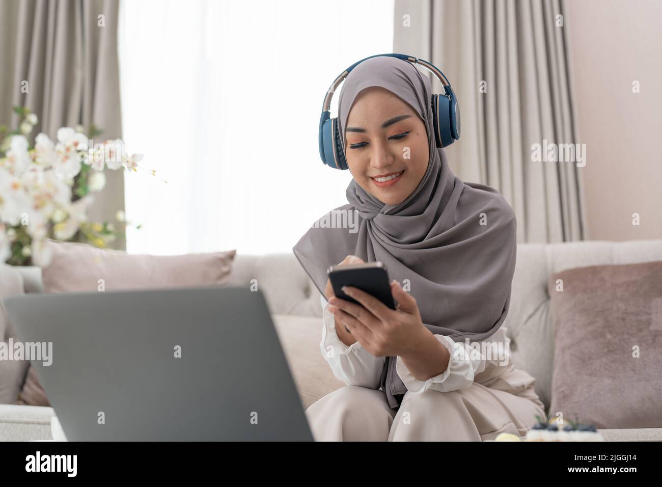 Muslimische Frau, die Mobiltelefon und Laptop benutzt und zu Hause im Büro sitzt Stockfoto