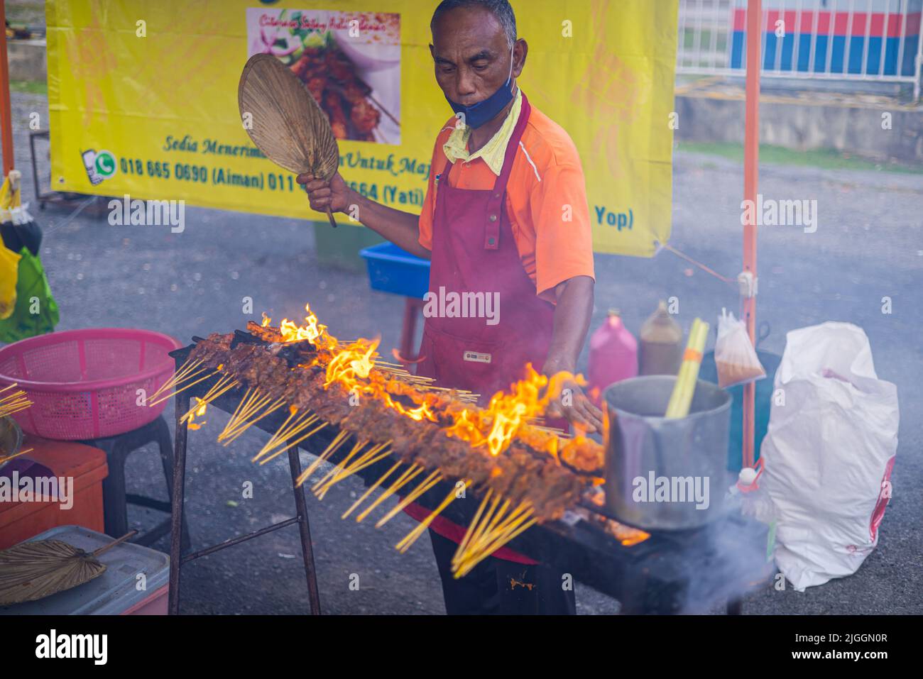 Kuala Lumpur, Malaysia - 21. Juni 2022: Alter Mann grillt satay über offenem Feuer auf einem Nachtmarkt. Sate ist ein gegrilltes Gericht, das ursprünglich aus Indonesien stammt, aber ve Stockfoto