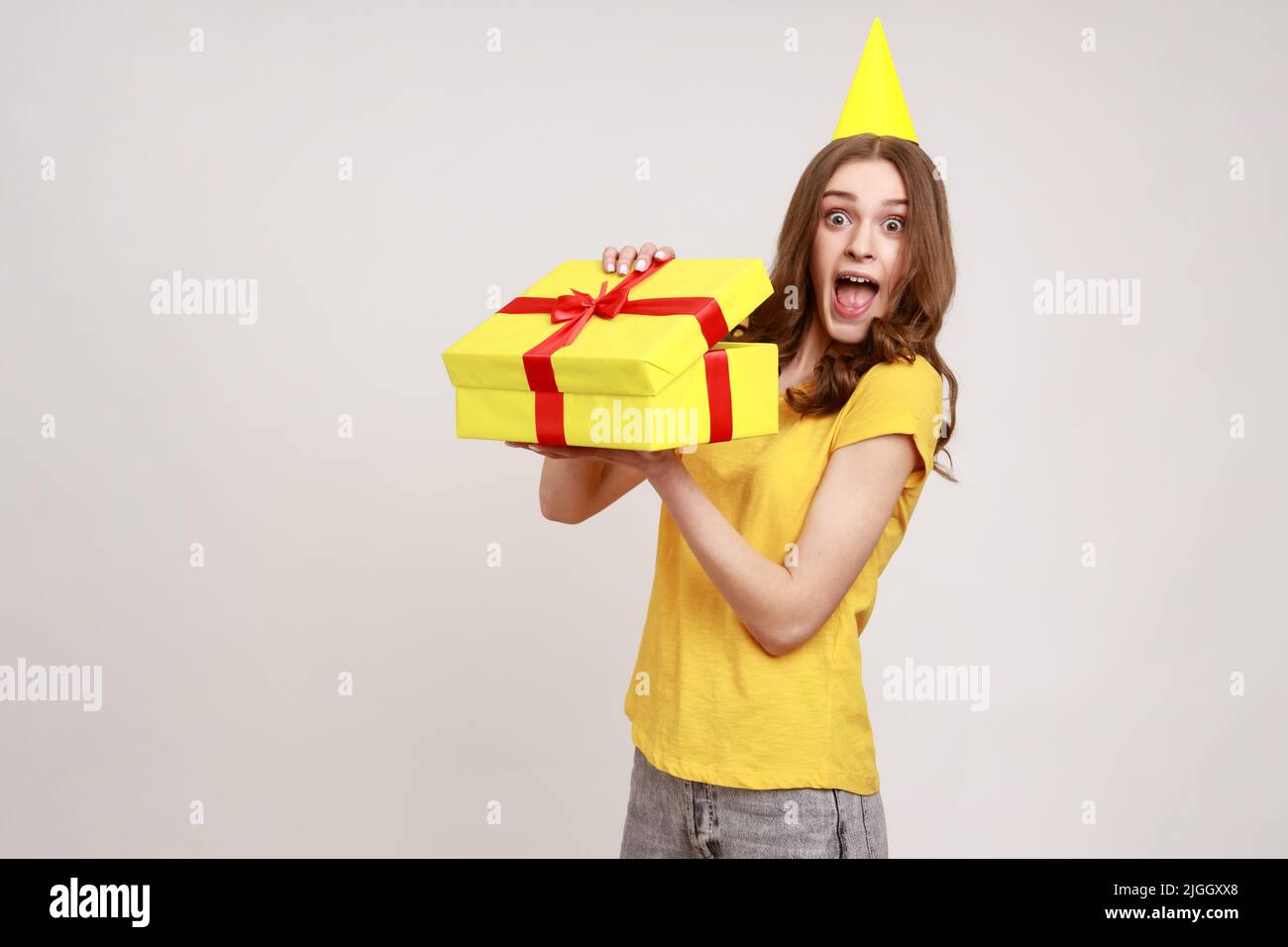 Porträt einer aufgeregten, verblüfften, braunhaarigen jungen Frau, die die Geschenkbox mit überraschter Ausstrahlung auspackte und das Geburtstagsgeschenk ausgepackt hatte. Innenaufnahme des Studios isoliert auf grauem Hintergrund. Stockfoto