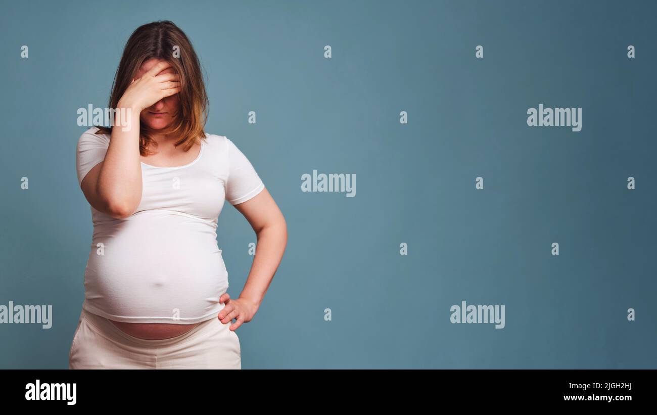 Nachgiebigkeit auf dem Gesicht einer Schwangeren, Studioaufnahme auf blauem Hintergrund, Kopierraum mit einem Platz unter dem Text über das Verbot von Abtreibungen Stockfoto