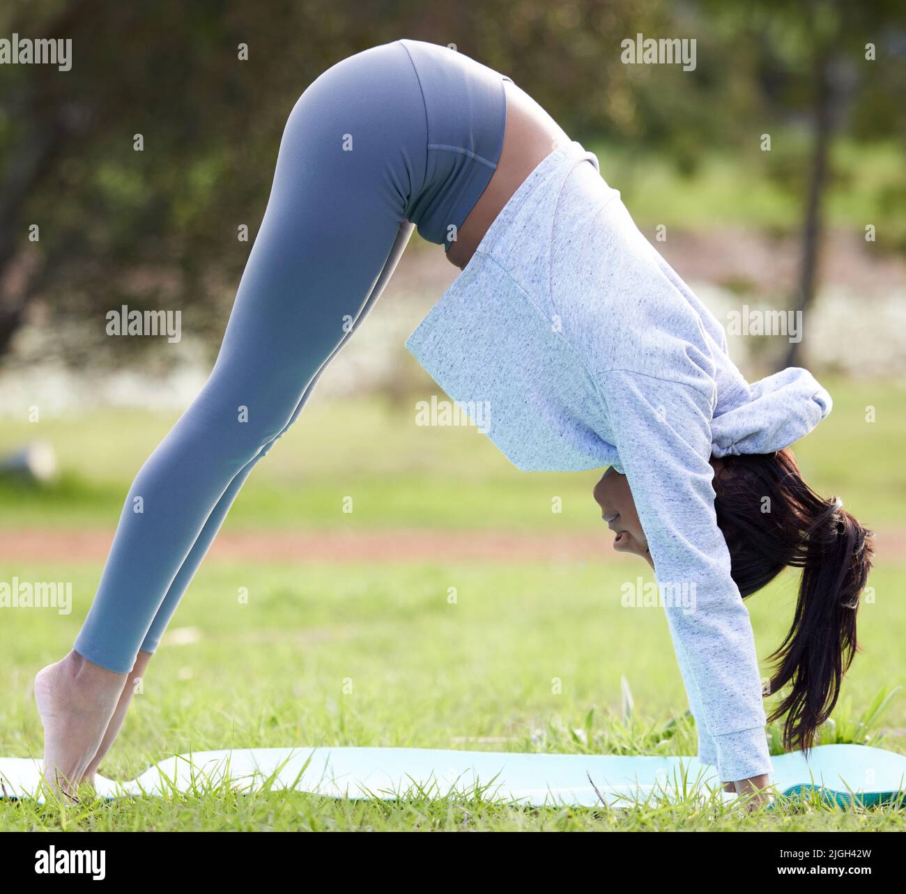 Eine junge Frau, die während ihrer Yoga-Routine im Park die Position des Hundes nach unten übt. Stockfoto